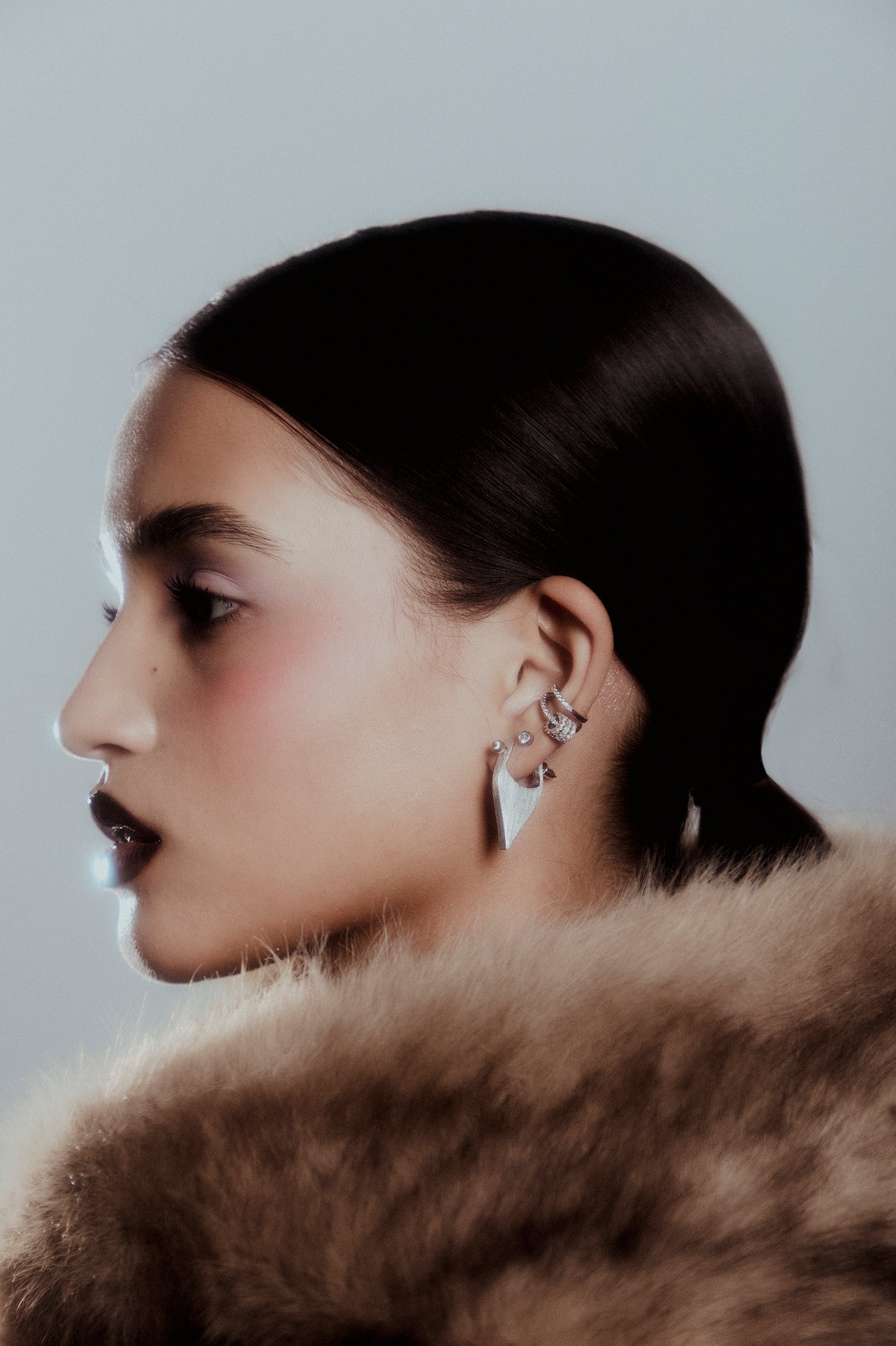 Close-up of a person wearing earrings with a fur collar against a plain background